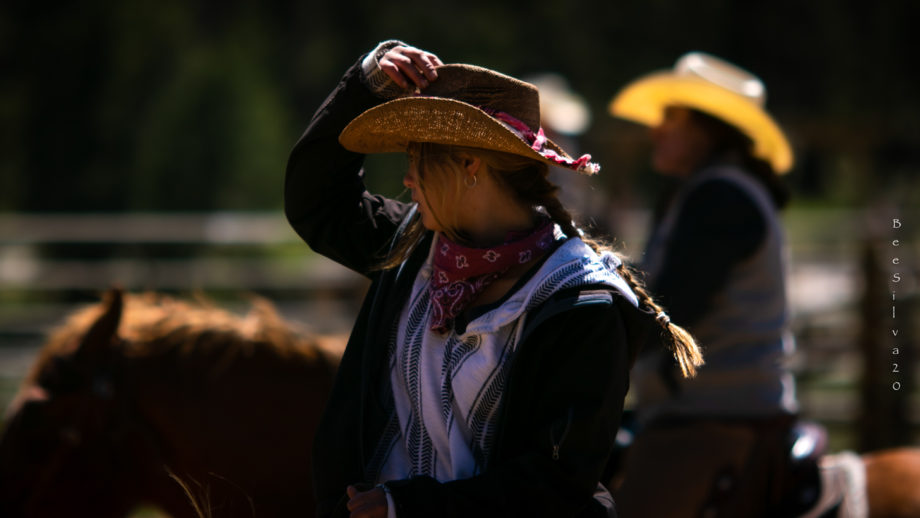 Woman adjusting her cowboy hat while riding a horse.