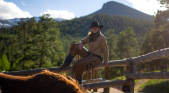 A woman balancing on fence wearing a cowboy hat.